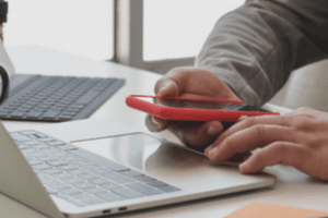 Man holding phone and sitting in front of a laptop